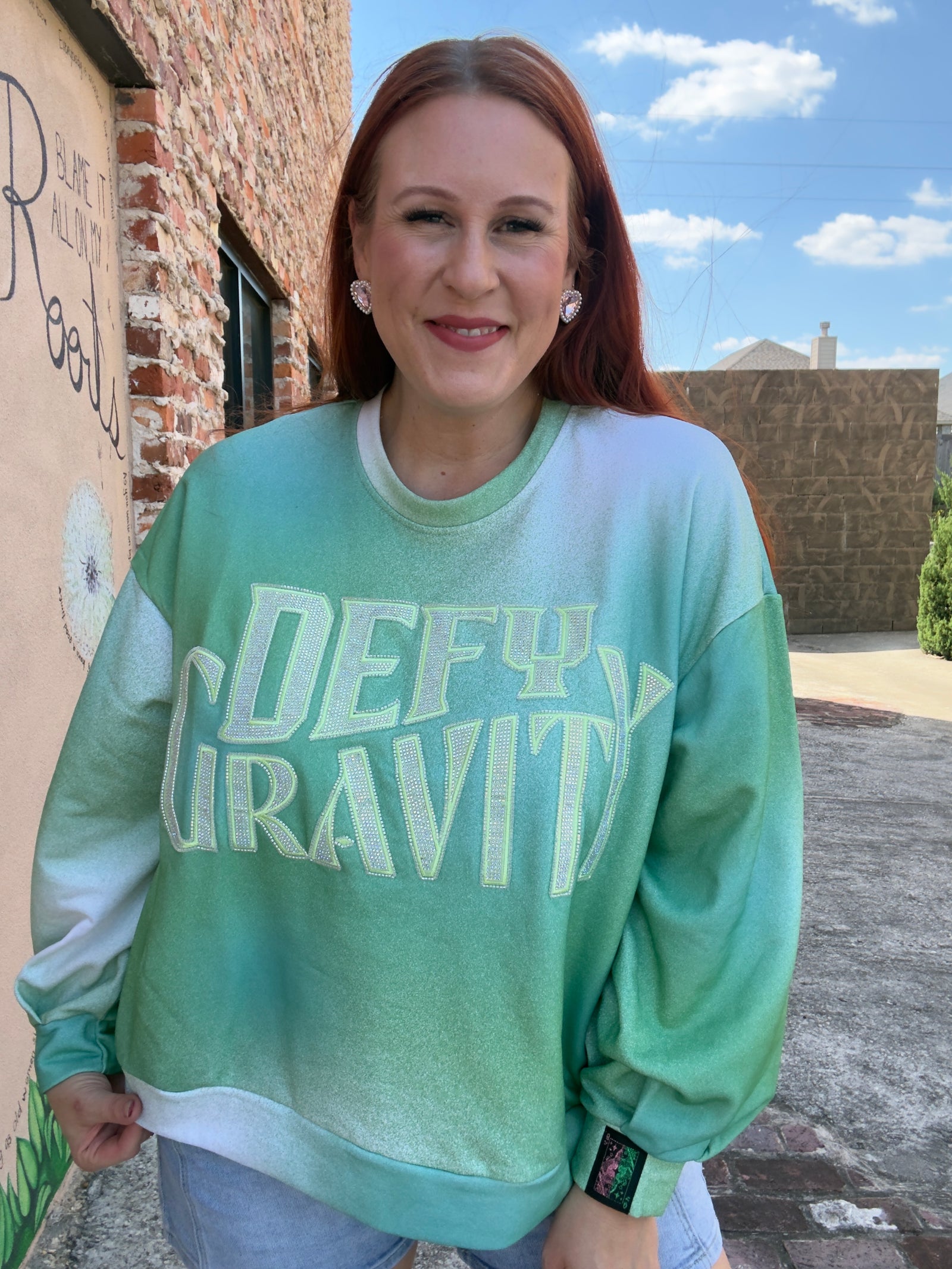 Woman wearing a green sweatshirt with 'DEFY GRAVITY' from the movie Wicked