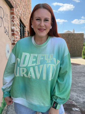 Woman wearing a green sweatshirt with 'DEFY GRAVITY' from the movie Wicked